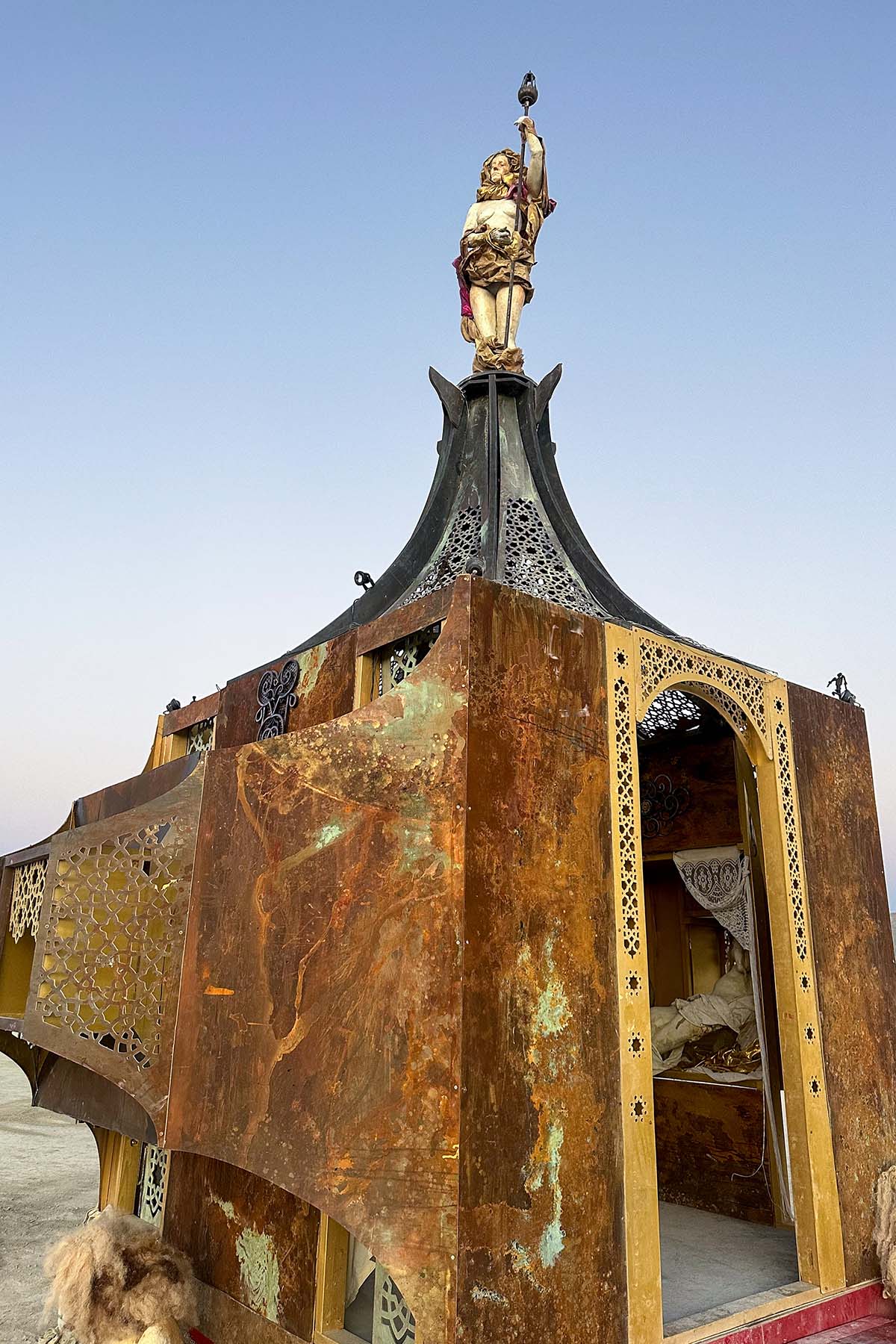 Low-angle view of the rusted metal pavilion and its pagoda-style roof, topped by a figure holding a torch aloft