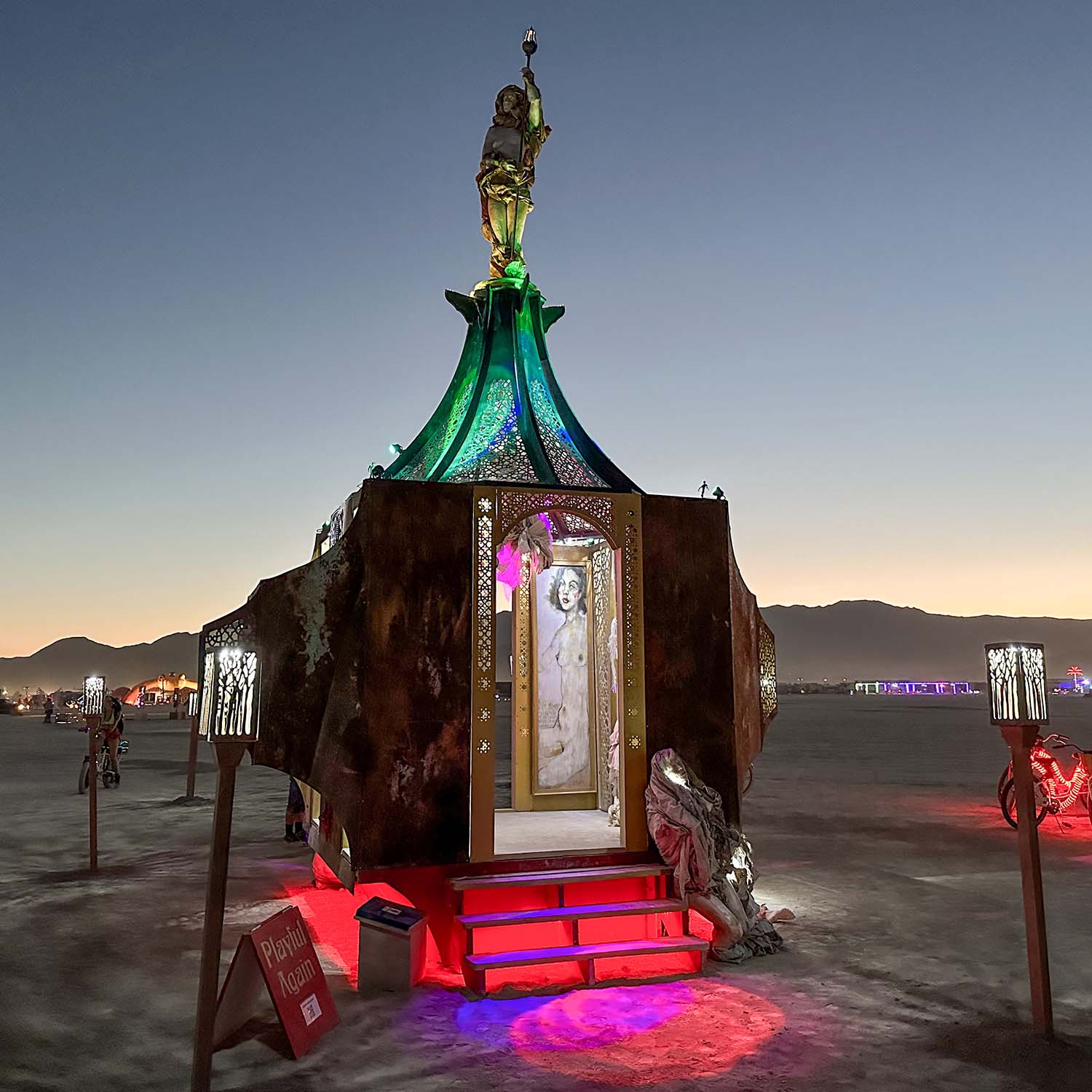 The pavilion at twilight with lantern posts, green roof lighting and colorful light on the playa