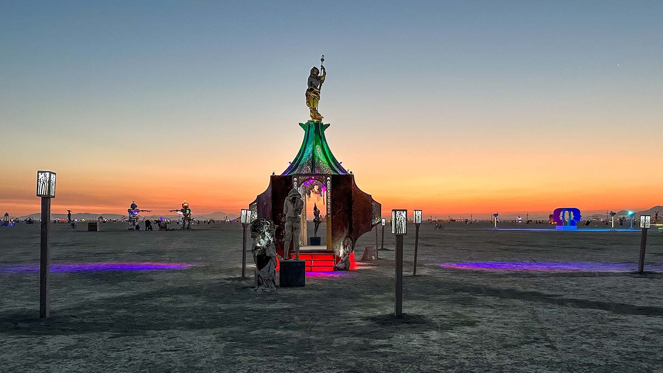 Playful Again in the distance at sunset, its lights glowing across the wide playa