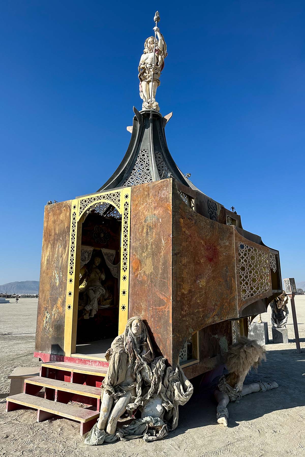 The rusted pavilion under a deep blue sky, with a seated figure near its steps