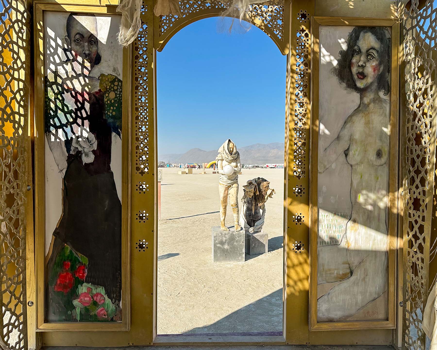 Painted portraits on either side of the doorway, framing a view of sculptures out on the playa