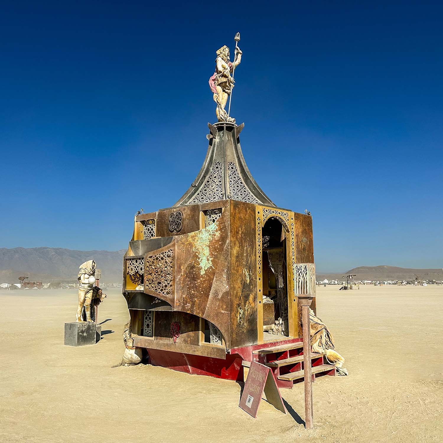 Side view of the rusted pavilion in daylight with a torch-bearing figure on top and red steps below