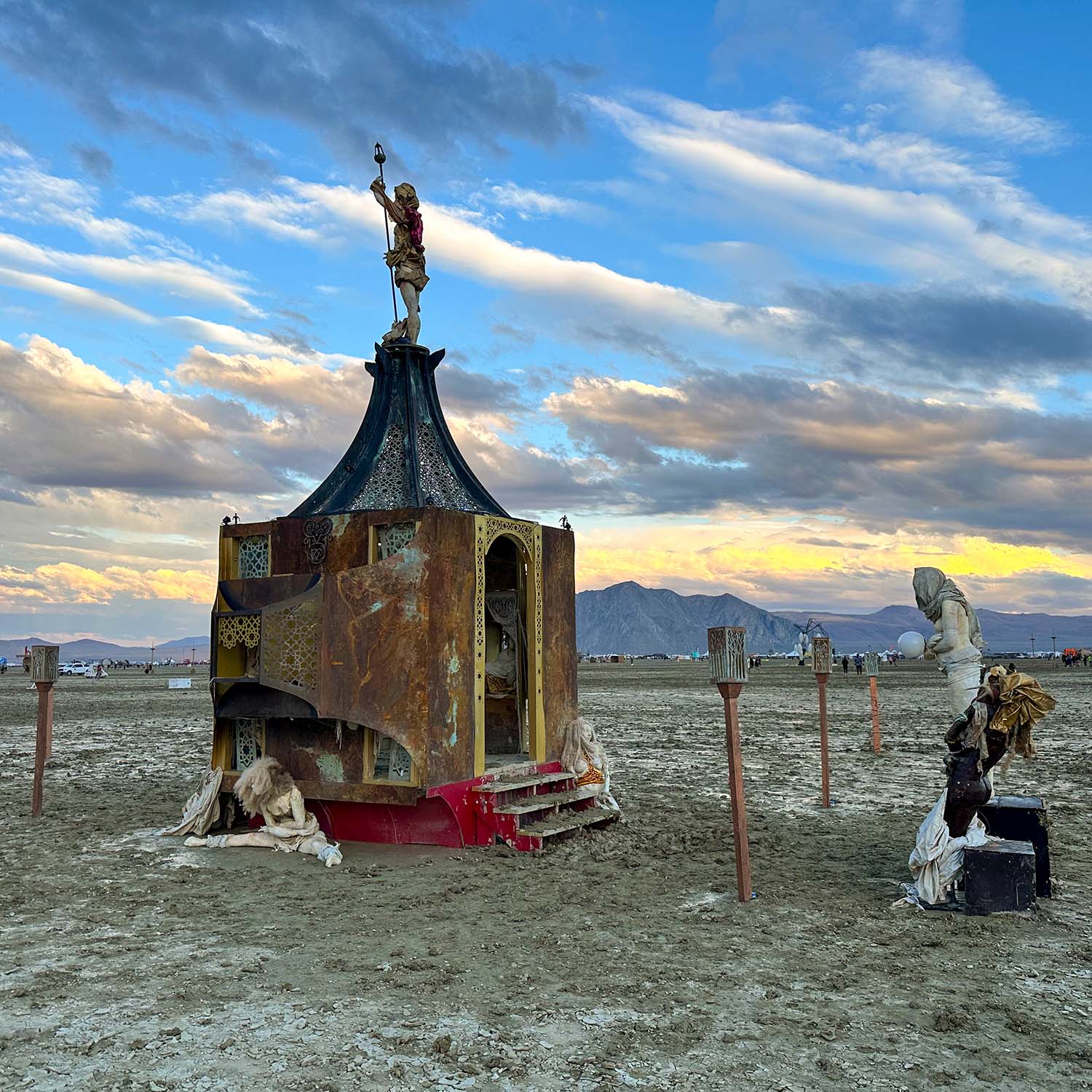 The pavilion beneath wispy clouds and blue sky, with figures gathered at its base